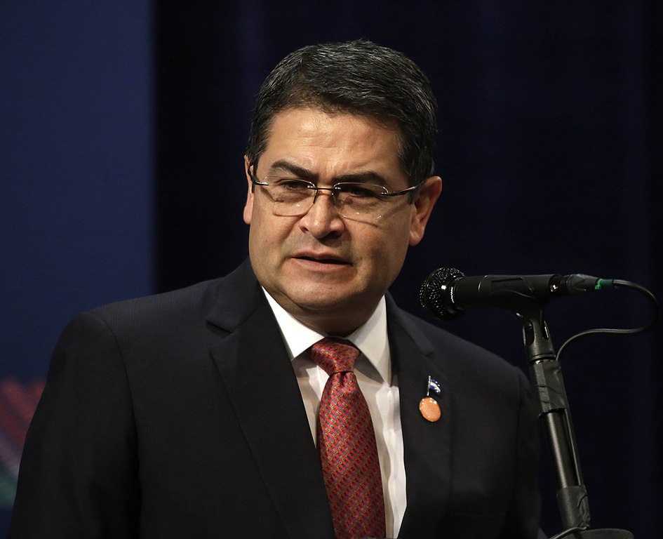 Juan Orlando Hernández, homem branco, de meia idade, cabelo curto preto, óculos de grau, vestindo terno escuro, com gravata vermelha e camisa branca