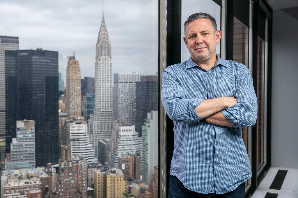 Phil Shawe, CEO of Trans Perfect, standing in front of a window with a cityscape background in his office on Park Avenue