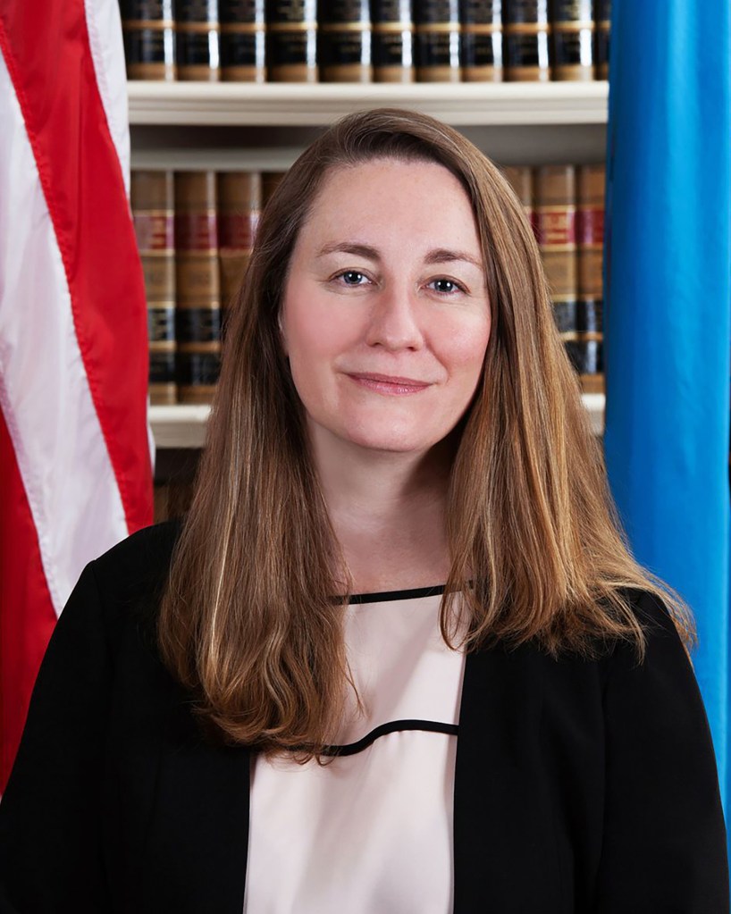 Kathaleen McCormick in judicial robes in front of bound leather books, an American flag and part of a blue flag.